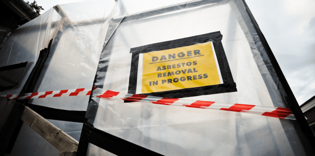 A containment area sealed with plastic sheeting and caution tape, featuring a yellow sign that reads "DANGER: ASBESTOS REMOVAL IN PROGRESS." This setup is used for safe asbestos abatement to prevent airborne contamination.
